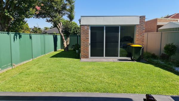 Mown back lawn beside a green fence and a brick studio