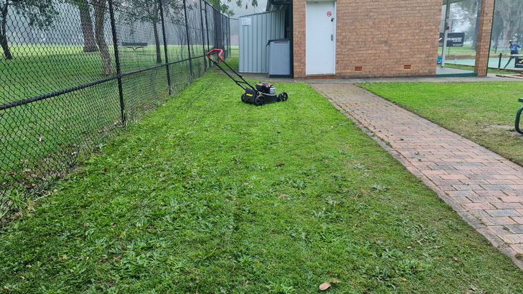 Lawn mower on grass beside a brick path and wire fence